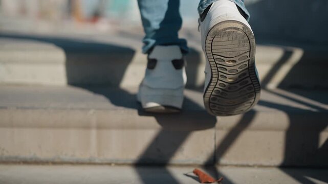 Woman legs and feet descend concrete steps wearing blue jeans and white sneakers. focus remains on lower body movement throughout sequence. Bright daylight casts distinct shadows from each