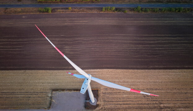 Aerial view of a wind turbine standing in a vast agricultural field with contrasting soil patterns and a road in the background in Vladimirovac, Vojvodina, Serbia.