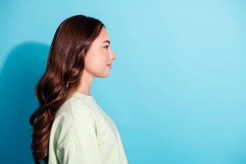 Young woman in profile with long hair standing against a bright blue background, calm studio portrait showing side view and natural expression © deagreez