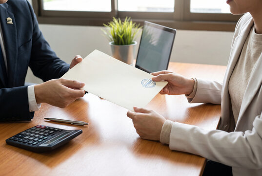 A lawyer or legal advisor hands over a document to a client, likely a legal contract or official paperwork, in a professional meeting setting with a laptop and calculator nearby.