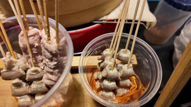 Close up shot of cooked meat and variety skewers served in clear plastic takeout cups at a traditional market in Thailand.
