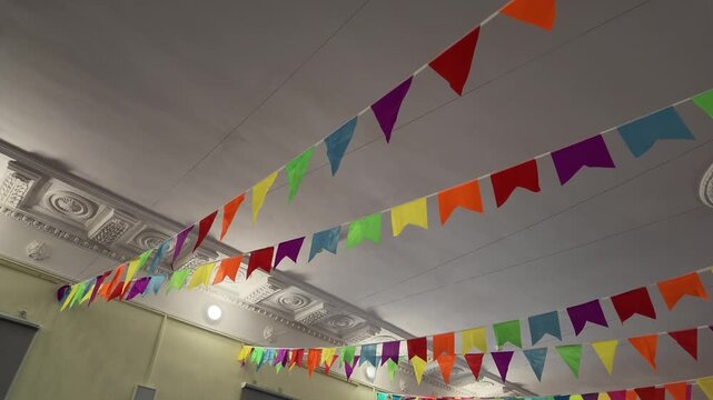 Colorful triangular festive bunting flags strung across ceiling, creating celebratory atmosphere for event or party.