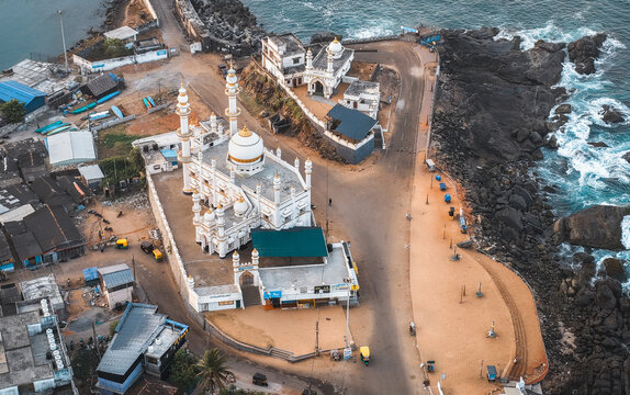 Aerial view of the white Vizhinjam Juma Masjid with its ornate minarets and domes situated along the rocky coastline of the Arabian Sea in Kovalam, Keralam, India.