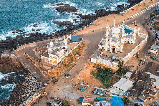 Aerial view of the Vizhinjam Juma Masjid along the rocky coastline, featuring white minarets, domes, coastal roads, and the blue waters of the Arabian Sea in Kovalam, Keralam, India.
