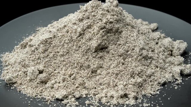 Mound of dry poppy seed filling mix rotating on black plate close up.