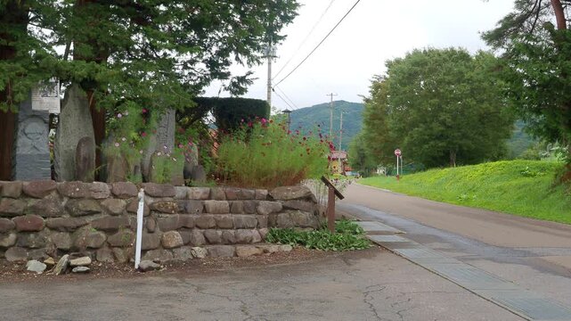 Horizontal video footage of a group of stone monuments in the Yamaguchi district of Tono City, Iwate, Japan. The camera slowly slides from right to left, moving from the surrounding rural mountain sce