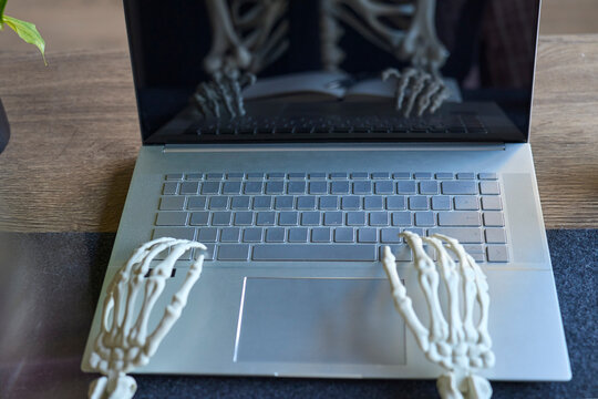 Skeleton hands positioned over laptop keyboard with reflection in dark screen