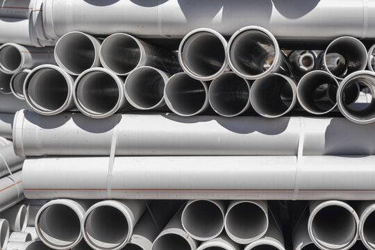 Stacked large grey plastic drainage pipes in a construction yard. This industrial image is ideal for construction, plumbing, infrastructure, and engineering projects.