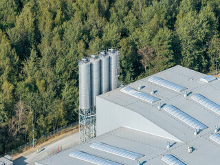 Industrial facility with storage silos near green forest, connecting nature and industry © Marcin