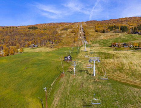 Aerial view of a ski lift stretching up a grassy mountainside covered in autumn foliage under a clear blue sky in Bjorli, Innlandet, Norway.
