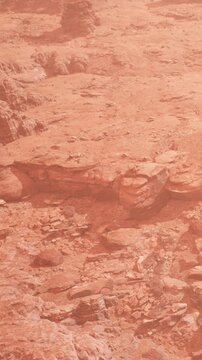 A barren landscape shows red rocks and stones scattered across the ground. The scene captures the dry, dusty hills in the background under bright sunlight.