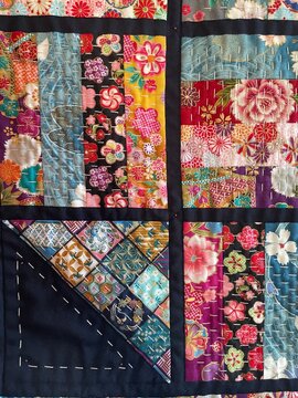 Close-up of a vibrant handmade Japanese-inspired patchwork quilt with colorful floral motifs and traditional white sashiko stitching