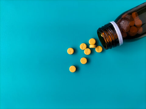 Yellow round tablets spilling out of an amber glass bottle