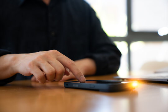 Close-up of a businessperson touching a smartphone on a desk beside a laptop, representing mobile technology, digital communication, online business and modern workplace connectivity.