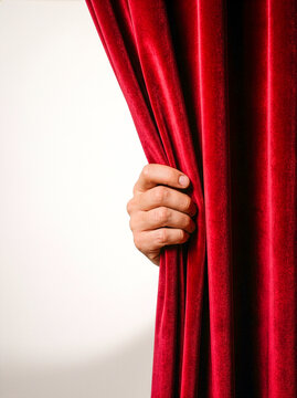 Hand pulling open red velvet theater curtain on white background