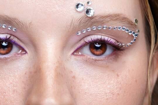 Young woman close-up creative eye makeup with glittering rhinestone crystals and purple eyeliner