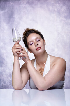 Serene female model holds wine glass containing pearls during surreal jewelry dining.
