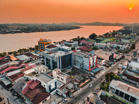 Samarinda, Indonesia - 21 September 2026: Aerial view of the BCA KCU Samarinda building by the Mahakam River, surrounded by urban rooftops, streets, and lush greenery under a sunset sky.