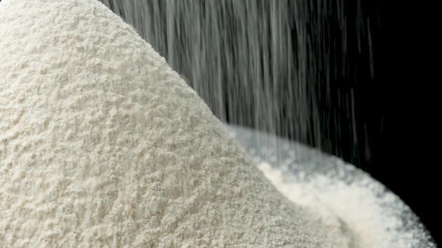 Organic whole grain spelt flour sifting onto mound on dark backdrop