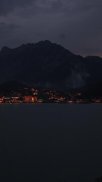 Vertical - Lakeside Town At Night With Illuminated Buildings Along Achen Lake In Tyrol, Austria. ascending drone shot