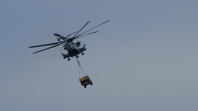 Large military helicopter flying with an armored truck hanging from below