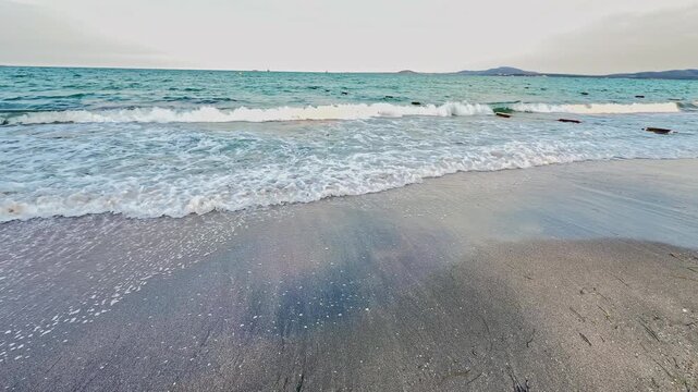 Waves come ashore at a beach with soft sand during sunset. The water reflects the light and creates patterns on the sand.