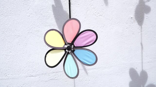 A colorful pinwheel with translucent petals casts a shadow on a textured white wall