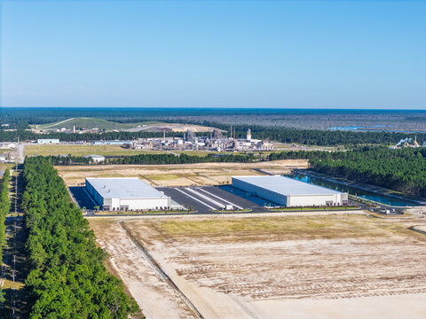 Wilmington, North Carolina, United States - 27 September 2026: Aerial view of two large modern warehouses in a developing industrial area surrounded by pine forests.