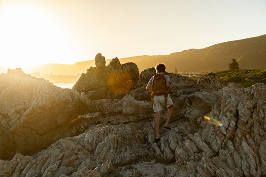 13 year old boy wearing backpack exploring the iconic rocky coastline of Kammabaai Beach, Hermanus, South Africa at sunset