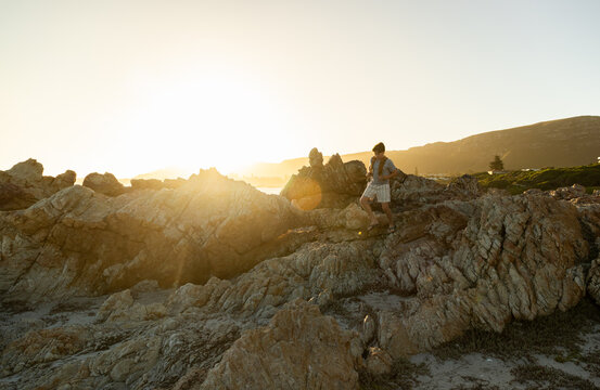 13 year old boy wearing backpack exploring the iconic rocky coastline of Kammabaai Beach, Hermanus, South Africa at sunset