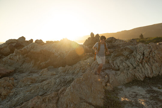 13 year old boy wearing backpack exploring the iconic rocky coastline of Kammabaai Beach, Hermanus, South Africa at sunset