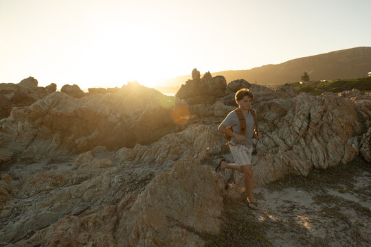 13 year old boy wearing backpack exploring the iconic rocky coastline of Kammabaai Beach, Hermanus, South Africa at sunset