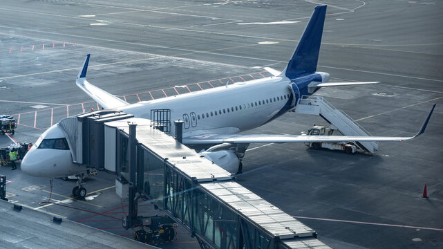 View of a commercial airplane parked at an airport gate connected to a jet bridge with a mobile staircase on the tarmac in Iceland.