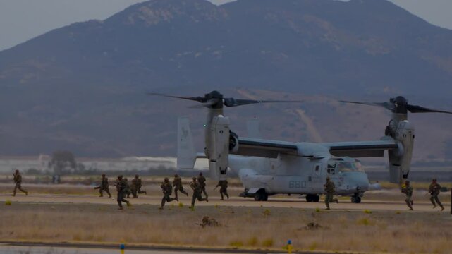 Military troops setting up for attack as an osprey does a vertical take off during a demonstration