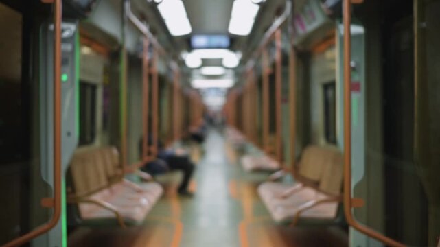 An blurred subway train interior shows a single person sitting on a seat. The passage is well-lit with rows of seats lined up along the sides, creating a spacious setting