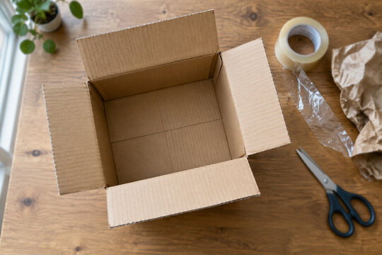 Top-down view of opened cardboard shipping box with tape and scissors.