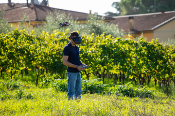 Naklejka premium Man flying FPV racing drone in vineyard
