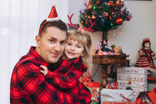 Portrait of a dad with his little daughter in matching Christmas clothes near a Christmas tree with gifts