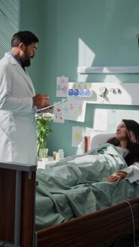 Doctor in white coat holds clipboard talking to woman patient