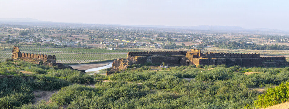 View of Rohtas Fort with its historic stone walls and battlements set against a green landscape and a winding stream in Dina, Punjab, Pakistan.