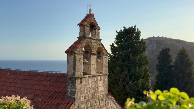 A beautiful view on Gradiste Monastery Church bell tower, Orthodox complex, Buljarica, Montenegro. Historic stone church bell tower with red tiled roof overlooking Adriatic Sea and coastal mountains