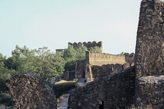 View of the historic stone walls and fortifications of Rohtas Fort surrounded by trees under a clear sky in Dina, Punjab, Pakistan.