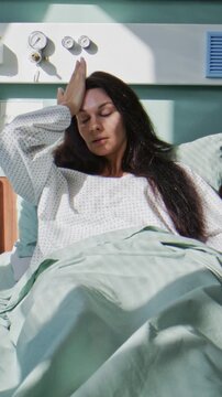 Woman feels headache as rests in soft bed in hospital ward