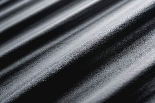 A close-up grayscale view of a corrugated metallic surface with parallel diagonal lines, showing texture and subtle light reflections.