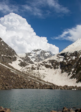 View of Jahaz Banda Lake surrounded by snow-capped mountains and rocky terrain under a blue sky with white clouds in Kumrat Valley, Khyber Pakhtunkhwa, Pakistan.