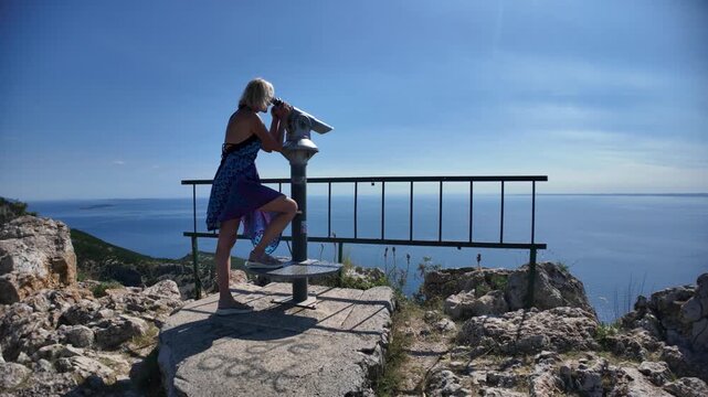 Woman standing on a high viewpoint at Lubenice village. Cres Island. Croatia. Looking through a coin-operated telescope the Sveti Ivan Beach