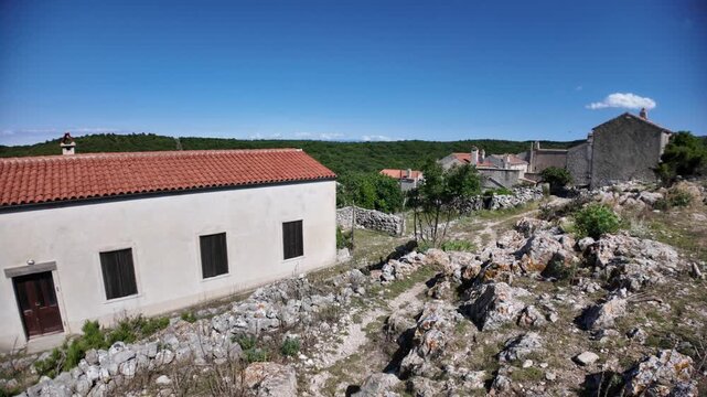 Lubenice village featuring traditional Mediterranean architecture and a stone bell tower, standing on a clear day with a vibrant blue sky over the green landscape of Cres Island in Croatia