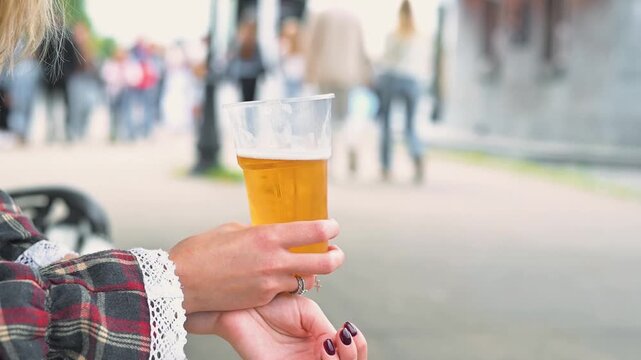 A person is holding a clear glass of beer with a golden color and light fizzy bubbles