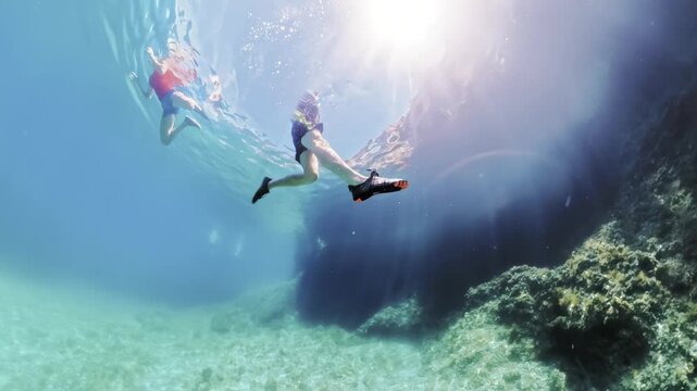 Two people are swimming and snorkeling underwater in the crystal-clear turquoise waters of Plava Grota Blue Cave on Cres Island, Croatia, with sunrays penetrating the surface