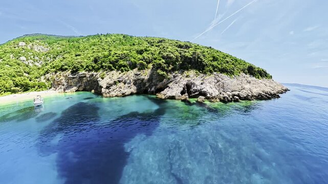 Plava Grota Blue Cave on Cres Island, Croatia, showing a rocky coastline with lush green vegetation, clear turquoise Adriatic Sea water, and a small boat near a sandy beach